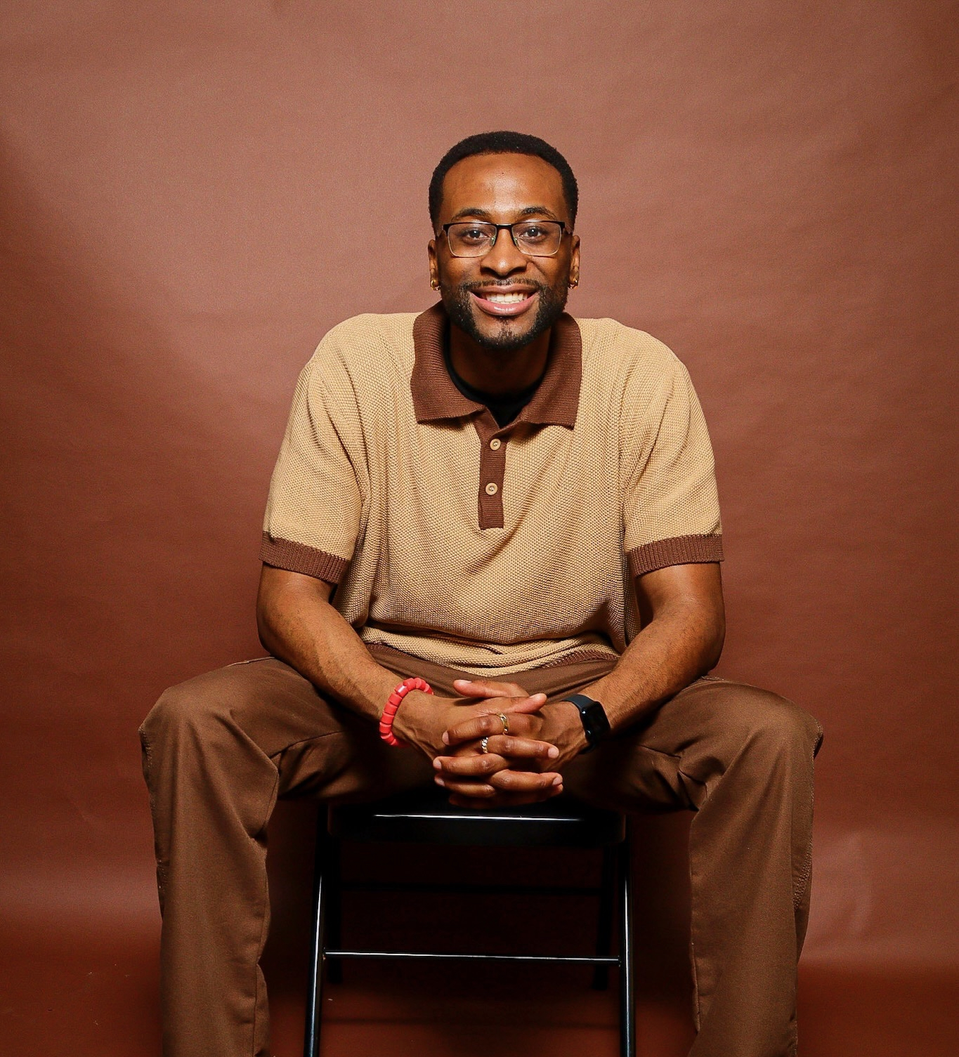 Brother Nnamdi seated in front of a terracotta studio backdrop, smiling at the camera